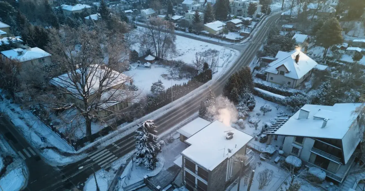 Zimowy krajobraz z dymem z komina, który może być oznaką, co to jest smog. Śnieg na dachach i drzewach.
